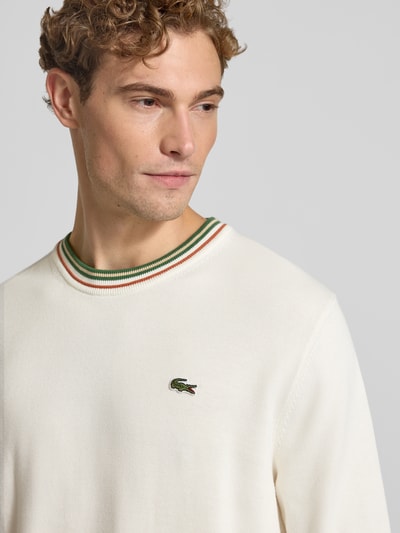 Männermodel trägt Regular Fit Pullover aus reiner Wolle von Lacoste in Creme mit farbigem Kragen, Nahaufnahme Oberkörper. Herren Pullover von Lacoste