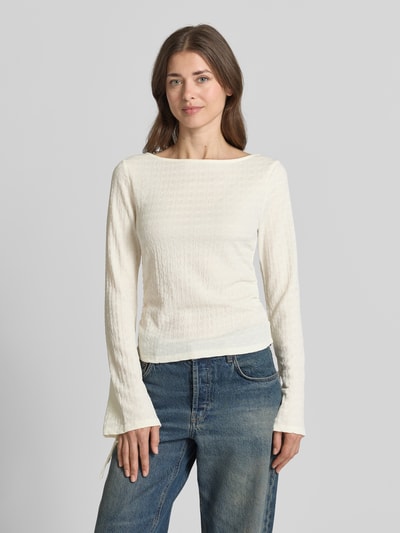 Frauenmodel trägt Regular Fit Langarmshirt mit Binde-Detail Modell 'HAZEL' von Vero Moda, unifarben, strukturierter Stoff, U-Boot-Ausschnitt, Trompetenärmel, Raffung, Farbe Creme, kombiniert mit blauen Jeans, Ganzkörperansicht von vorne.