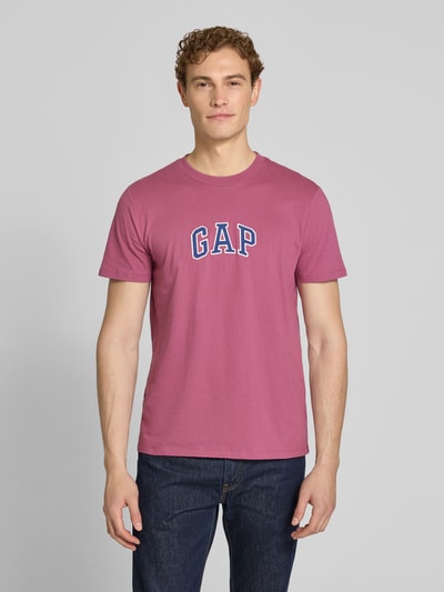 Männermodel trägt GAP T-Shirt mit Logo-Patch und Rundhalsausschnitt in Rosa, reine Baumwolle, Straight Fit, Ganzkörperansicht von vorne.