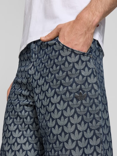 Männermodel trägt Wide Fit Jeans mit Eingrifftaschen von adidas Originals in Blau mit Allover-Muster, reine Baumwolle, Nahaufnahme Oberschenkel.