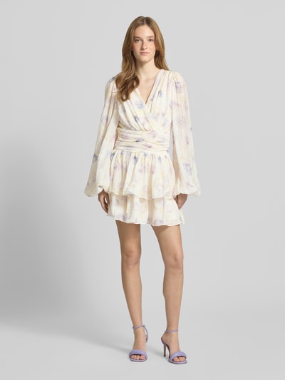 Frauenmodel trägt Minikleid aus Viskose-Mix mit V-Ausschnitt von Gina Tricot, floraler Allover-Print, Taillierte Passform, Langärmelig, Raffungen, helle Pastellfarben, fließende Textur, Rückenlänge 84 cm, Brustweite 42 cm, Ärmellänge 70 cm, Ganzkörperansicht von vorne.