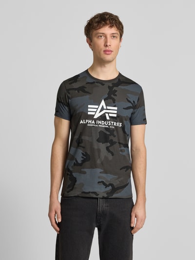 Männermodel trägt T-Shirt mit Label-Print von Alpha Industries, Herren T-Shirt aus Reine Baumwolle, Gerader-Schnitt, Rundhalsausschnitt, Rückenlänge bei Größe M 70 cm, Camouflage-Muster, Ganzkörperansicht von vorne