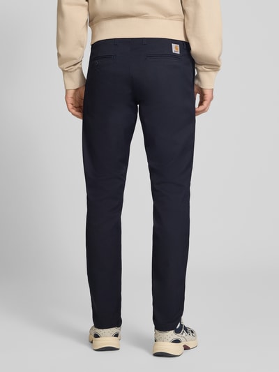 Männermodel trägt Skinny Fit Hose aus Baumwoll-Mix Modell 'SID' von Carhartt Work In Progress in Dunkelblau, Ganzkörperansicht Rückansicht. Bundweite 45 cm, Innenbeinlänge 79 cm, Seiten- und Gesäßtaschen.