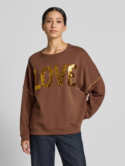 Frauenmodel trägt Oversized Sweatshirt aus reiner Baumwolle Modell 'LOVE' von miss goodlife in Braun mit Pailletten und Statement-Print, Ganzkörperansicht von vorne.