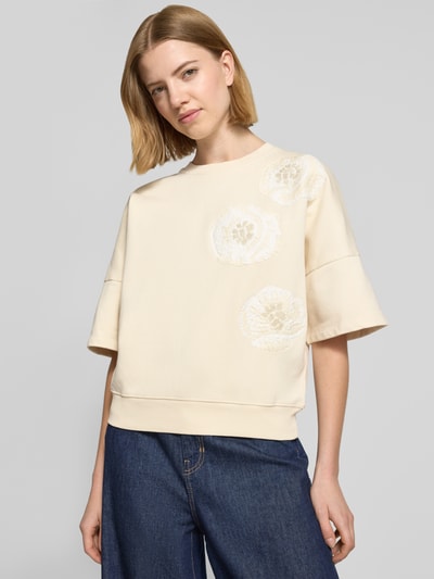 Frauenmodel trägt Sweatshirt mit 1/2-Arm Modell 'MINDULI' von Drykorn aus reiner Baumwolle, lose geschnitten, helle Farbe, florales Motiv-Stitching, gerippter Rundhalsausschnitt, Nahaufnahme Oberkörper.