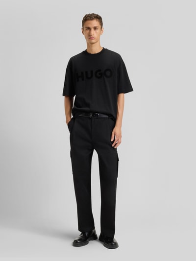 Männermodel trägt Oversized T-Shirt aus reiner Baumwolle Modell 'DINKEE' von HUGO in Schwarz, Unifarben, Label Print, Ganzkörperansicht von vorne.