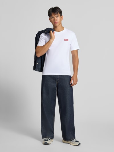 Männermodel trägt Regular Fit T-Shirt aus reiner Baumwolle mit Label-Detail von JACK & JONES, weiß, kombiniert mit dunkler Jeans, Ganzkörperansicht von vorne. Rückenlänge bei Größe M: 67 cm, Rundhalsausschnitt.