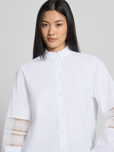 Frauenmodel trägt Regular Fit Bluse aus Baumwoll-Mix Modell 'Gala' von MANGO, weiß, Stehkragen mit Rüschen, Loch-Stitching, Nahaufnahme Oberkörper.
