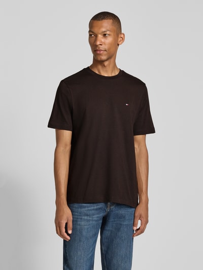 Männermodel trägt Regular Fit T-Shirt aus reiner Baumwolle von Tommy Hilfiger in Schwarz, kombiniert mit blauer Jeans, Ganzkörperansicht von vorne. Herren T-Shirt von Tommy Hilfiger.
