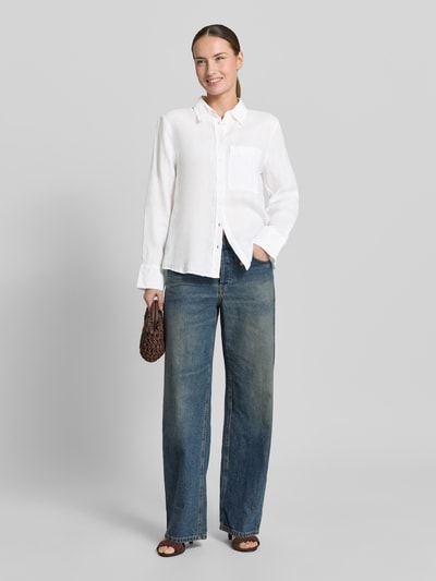Frauenmodel trägt Leinenbluse mit Brusttasche Modell 'LINO' von Mango in Weiß, Loose-Fit, Kentkragen, Knopfleiste, Sportmanschetten, Rückenlänge bei Größe S 67 cm, Ärmellänge 59 cm, Jeans, schlichte Texturen, Ganzkörperansicht von vorne.