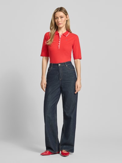 Frauenmodel trägt Slim Fit Poloshirt aus Lyocell-Mix von Tommy Hilfiger, Optik: Unifarben, Passform: Slim-Fit, Logo-Stitching, Kontraststreifen, Verschluss: Knopfleiste, 1/2-Arm, Materialverarbeitung: Piqué, Ganzkörperansicht von vorne.