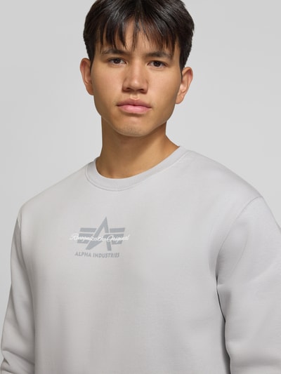Männermodel trägt Regular Fit Sweatshirt aus Baumwoll-Mix mit Label-Detail von Alpha Industries, glatte Struktur, hellgrau, Nahaufnahme Oberkörper.