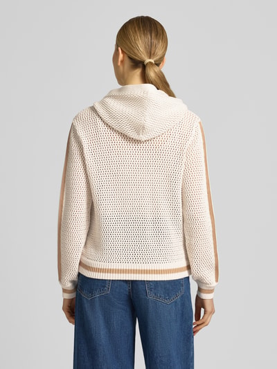 Frauenmodel trägt Regular Fit Strickjacke mit Kapuze von monari aus Reine Baumwolle mit Lochmuster, Logo-Detail, Zierbesatz, AufgesetzteTaschen, Elastische Abschlüsse, durchgängige Knopfleiste, beige und cremefarben kombiniert, Rückenlänge 56 cm, Ärmellänge 59 cm, Ganzkörperansicht Rückansicht.