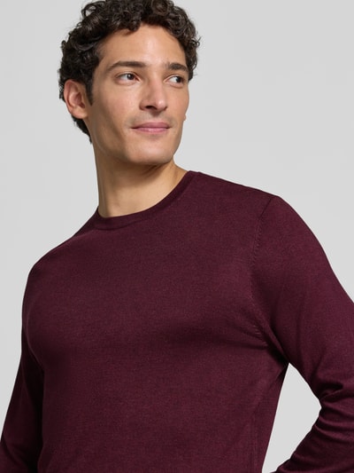Männermodel trägt Strickpullover mit geripptem Rundhalsausschnitt von MCNEAL in Burgunder, glatte Textur, Nahaufnahme Oberkörper. Taillierte Passform, leicht überschnittene Schultern, gerippte Abschlüsse.
