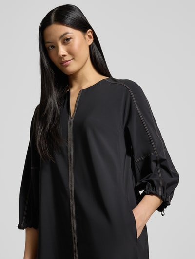 Frauenmodel trägt Knielanges Kleid mit V-Ausschnitt von Marc Cain in Schwarz, Elastischer-Material-Mix, Lockerer-Schnitt, 3/4-Arm, Nahaufnahme Oberkörper.