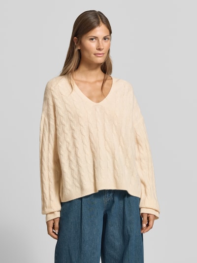 Frauenmodel trägt Relaxed Fit Pullover aus reiner Baumwolle von MYON in Creme, Strick-Optik, V-Ausschnitt, Langarm, Ganzkörperansicht von vorne.