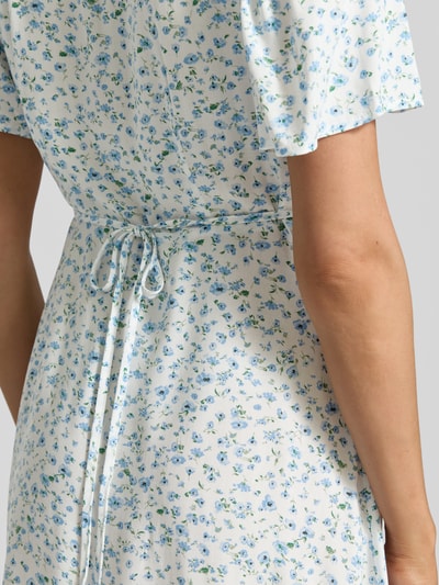 Frauenmodel trägt Leicht ausgestelltes Minikleid aus reiner Viskose Modell 'ALBA' von Vero Moda mit blauem Blumenmuster, Nahaufnahme Rückansicht.