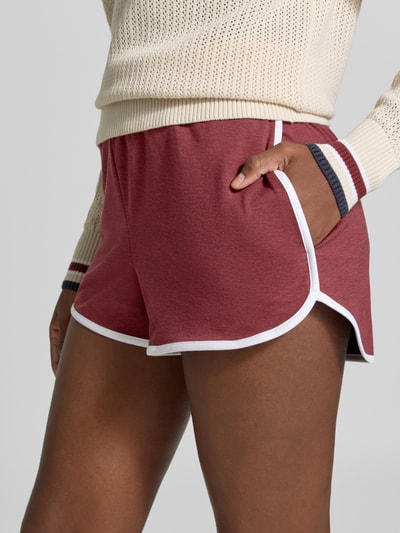 Frauenmodel trägt Regular Fit Shorts mit elastischem Bund Modell 'Marty' von VARLEY in Rot mit weißer Paspel, Nahaufnahme Oberschenkel, elastischer Material-Mix, verlagerte Rückseite, Damen Shorts