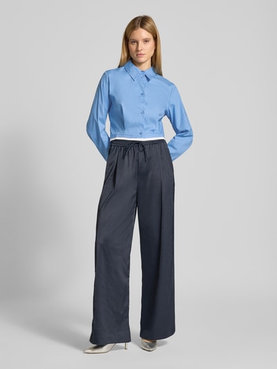 Frauenmodel trägt Cropped Hemdbluse mit gelegten Falten Modell 'Zopy' von Gestuz aus elastischem Baumwoll-Mix, hellblau, Ganzkörperansicht von vorne.
