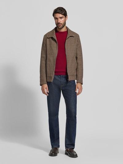 Męski model nosi Regular Fit Pullover aus reiner Wolle od GANT w kolorze czerwonym, ciemne dżinsy, widok całej sylwetki z przodu.