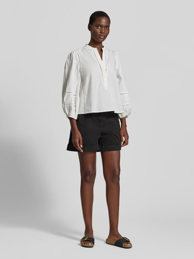 Frauenmodel trägt Relaxed Fit Shorts aus Baumwoll-Mix Modell 'TANESSA-D' von BOSS Orange in Schwarz, unifarben mit Logo-Stitching, seitliche Eingrifftaschen und Gürtelschlaufen, kombiniert mit weißer Bluse, Ganzkörperansicht von vorne.