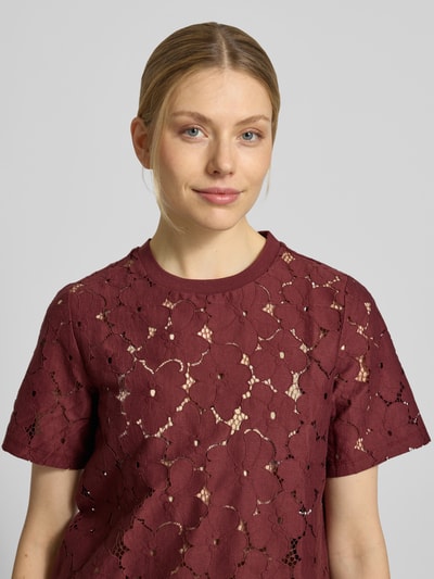 Kobieta modelka nosi Regular Fit T-Shirt aus Spitze Modell 'SALLIE' od Vero Moda, bordowy, bawełniany mix, krótki rękaw, gładki, dekolt okrągły, krój regular fit, faktura koronkowa, zbliżenie na górną część ciała.