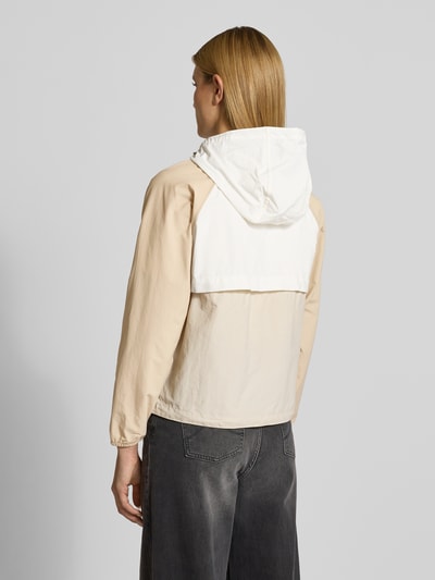 Frauenmodel trägt Windbreaker mit Rückenbelüftungssystem und Kapuze von Columbia in Beige und Weiß, Wasserabweisend, Lockerer-Schnitt, Ganzkörperansicht Rückansicht.