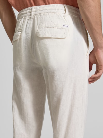 Mężczyzna nosi Hose aus Leinen-Baumwoll-Mix mit elastischem Bund von Lindbergh, kolor jasny beż, krój regular fit, wejściowe kieszenie, szerokość w rozmiarze M 40 cm, długość nogawki 79 cm, tekstura lekko ziarnista, widok całej sylwetki z tyłu.