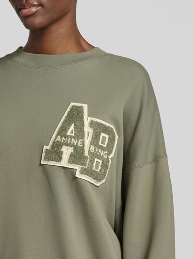 Frauenmodel trägt Relaxed Fit T-Shirt mit Logo-Print von Anine Bing in Olivgrün aus reiner Baumwolle mit Rundhalsausschnitt und eingefassten Ärmelabschlüssen, Nahaufnahme Oberkörper