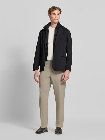 Männermodel trägt Regular Fit Jacke mit Stehkragen von Emporio Armani in Schwarz, glatte Textur, Ganzkörperansicht von vorne. Elastischer Material-Mix, Reverskragen, Reißverschluss, 2-Knopfleiste, Brusttasche, Paspeltaschen, beige Hose, neutrale Farbtöne.