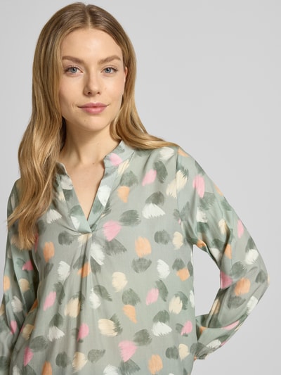 Frauenmodel trägt Regular Fit Bluse aus reiner Viskose Modell 'Hilga' von ZABAIONE, hellgrüner Stoff mit buntem Muster, Tunika-Kragen, elastische Ärmelabschlüsse, Nahaufnahme Oberkörper.