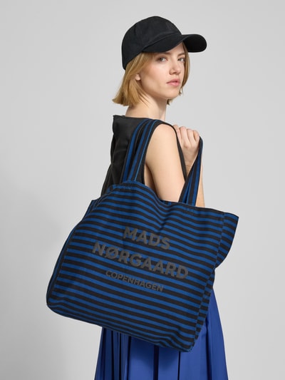 Frauenmodel trägt Shopper aus Baumwolle mit Logo Modell 'Boutiqno Athene' von MADS NØRGAARD, blau-schwarze Streifen, offene Struktur, Tragehenkel, Ganzkörperansicht Rückansicht.