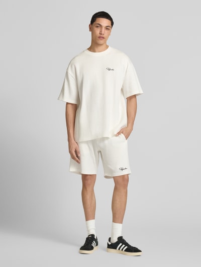 Männermodel trägt Shorts mit Logo-Stitching und elastischem Bund von Pegador in Creme, Reine Baumwolle, Loose-Fit, Ganzkörperansicht von vorne.