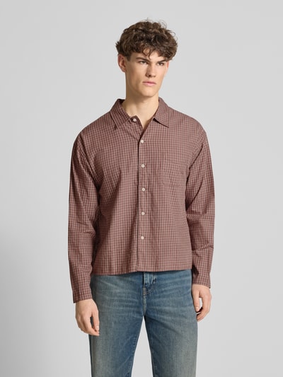 Męski model nosi Regular Fit Freizeithemd mit Kentkragen od Jack & Jones z bawełny ekologicznej, model 'AUSTIN', krój regular fit, kołnierzyk typu kent, brustasza, listwa guzikowa, długość tyłu w rozmiarze M: 67 cm, szerokość w rozmiarze M: 56 cm, długość rękawów w rozmiarze M: 60 cm, wzór kratka, odcienie brązu, tkanina gładka, widok całej sylwetki z przodu.