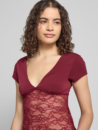 Frauenmodel trägt T-Shirt mit V-Ausschnitt und Spitze von Gina Tricot in Bordeaux, Material-Mix mit Stretch-Anteil, Slim-Fit, Rückenlänge 51 cm, Nahaufnahme Oberkörper.