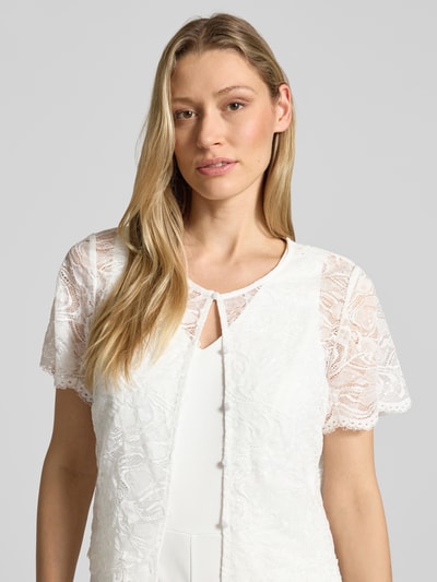 Modelka nosi Regular Fit Jumpsuit mit Spitzenbesatz od Vera Mont, elastyczna mieszanka materiałów, cekinowe obszycie, z krótkim rękawem, listwa guzikowa, okrągły dekolt, kolor biały, tkanina z koronkową teksturą, szerokość w rozmiarze 36: 47 cm, długość tyłu: 50 cm, całkowita długość: 157 cm, długość rękawów: 20 cm, długość wewnętrzna nogawki: 81 cm, z przodu zbliżenie na górną część ciała.