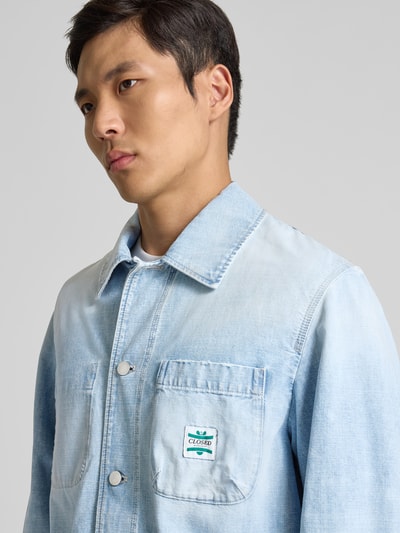 Männermodel trägt Relaxed Fit Hemdjacke in Denim-Optik von Closed aus reiner Baumwolle, aufgesetzte Taschen, Knopfleiste, Nahaufnahme Oberkörper.