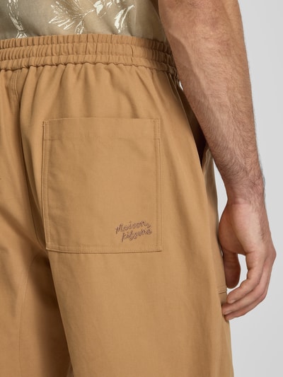Männermodel trägt Straight Fit Stoffhose aus Baumwolle von MAISON KITSUNÉ in Beige mit elastischem Bund und Gesäßtasche, Nahaufnahme Rückansicht.