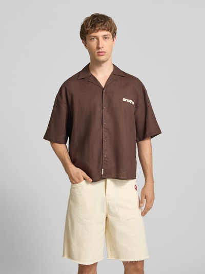 Męski model nosi Relaxed Fit Leinenhemd mit Label-Stitching od ANOTHER COTTON LAB, len, kołnierz z połami, listwa guzikowa, detal z logo, brązowy, długość tyłu 70 cm, szerokość ramion 43 cm, długość rękawów 35 cm, widok całej sylwetki od przodu.