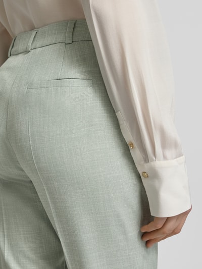 Vrouwenmodel draagt Slim Fit Stoffhose aus Viskose-Mix mit Bügelfalten van comma in lichtgroen, materiaal met fijne structuur, met elastische viscosemix, biesplooien, achterzak en haak- en ritssluiting, detailopname heup- en taillebereich.