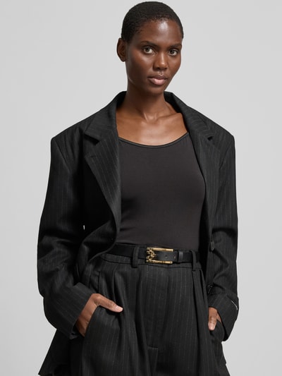 Frauenmodel trägt Damen Gürtel mit Dornschließe von Victoria Beckham mit Strukturmuster, Logo-Detail und glänzender Optik, Nahaufnahme Oberkörper.