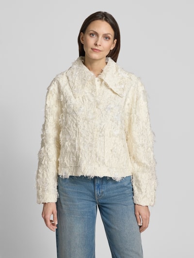 Modelka nosi kurtkę z mieszanki wiskozy z frędzlami model 'JANY' od Copenhagen Muse, krój regular fit, wykładany kołnierz, kolor kremowy, długość tyłu 54 cm, szerokość ramion w rozmiarze S 46 cm, szerokość klatki piersiowej w rozmiarze S 51 cm, długość rękawów 60 cm, faktura nieregularna, całość jasna, widoczny przód, zdjęcie w ujęciu całej sylwetki z przodu.