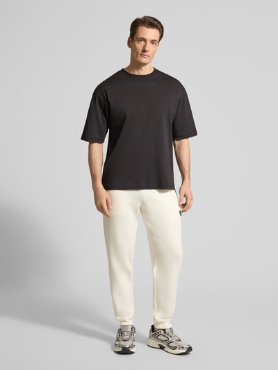 Männermodel trägt Sweatpants mit Viskose-Anteil Modell 'TRAIN PREMIUM SHIELD' von EA7 Emporio Armani in Creme mit geradem Schnitt, Ganzkörperansicht von vorne.