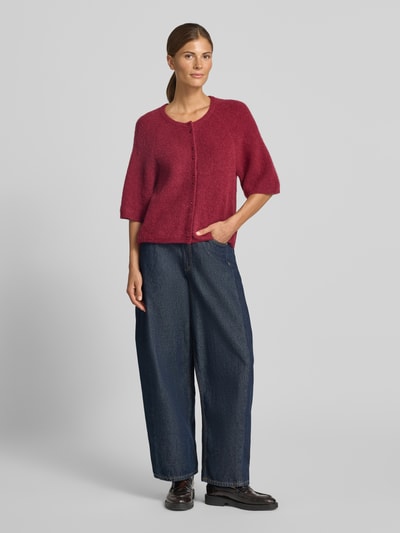 Frauenmodel trägt Strickweste mit 1/2-Arm Modell 'Bondie Hope' von MSCH Copenhagen in Dunkelrot, Regular Fit, mit Knopfleiste, Kombi aus Wolle, Rundhalsausschnitt, Halbarm, gerade Form, getragen zu weiter blauer Denim-Hose und schwarzen Schuhen, Haptik leicht flauschig, Ganzkörperansicht von vorne.