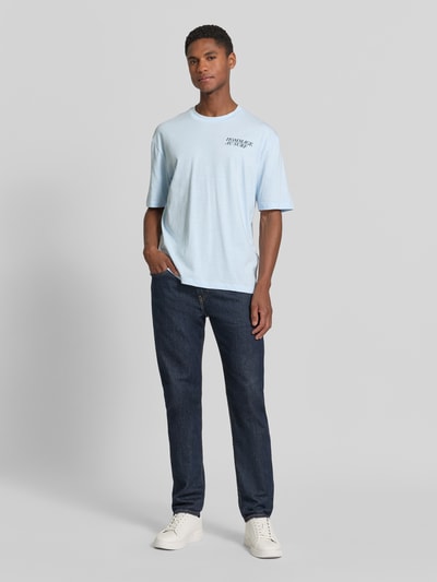 Mannenmodel draagt Regular Fit T-shirt aus Baumwoll-Mix van s.Oliver RED LABEL in look: effen kleuren, katoenmix, korte mouw, ronde hals, opschrift-applicatie, jersey materiaal, lichte blauwe tint, gladde textuur. Volledige lichaamsvoorzijde.