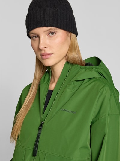 Vrouwenmodel draagt Jacke mit Pattentaschen Modell 'MILENA' van Didriksons in groen met capuchon, recht pasvorm, labelprint, detailopname gezicht/bovenlichaam.