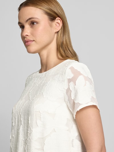 Modelka kobieca ma na sobie Blusenshirt aus Viskose-Mix mit Strukturmuster od More & More, kolor biały, okrągły dekolt, prosty krój, wzór strukturalny, długość tyłu w rozmiarze 36: 56 cm, długość rękawa w rozmiarze 36: 18 cm, zbliżenie na górną część ciała z przodu