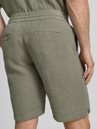 Männermodel trägt Shorts mit Eingrifftaschen und elastischem Bund von Lindbergh in Oliv, Reine Baumwolle, Loose-Fit, Ganzkörperansicht Rückansicht.