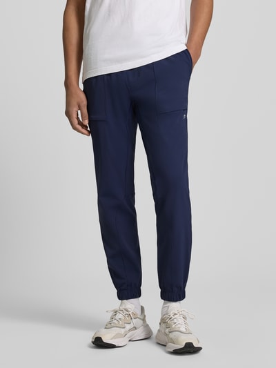 Männermodel trägt Slim Fit Jogger mit elastischem Bund von Fabletics, Elastischer-Material-Mix, Eingrifftaschen, Ganzkörperansicht von vorne.
