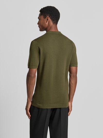 Męski model nosi Slim Fit Poloshirt mit kurzer Knopfleiste Modell 'TRITON' von Drykorn, czysta bawełna, krój slim fit, kolor oliwkowy, tekstura siateczki, długość tyłu w rozmiarze M 69 cm, Ganzkörperansicht Rückansicht.